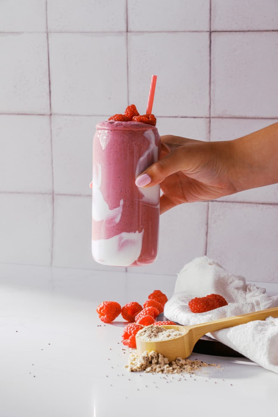 A hand holding a raspberry smoothie with cream swirls.